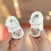 A pair of white soft sole first walker shoes featuring a cute bear design, held in a person's hands.