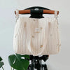 A cream quilted diaper bag with embroidery hangs on a black stroller frame.
