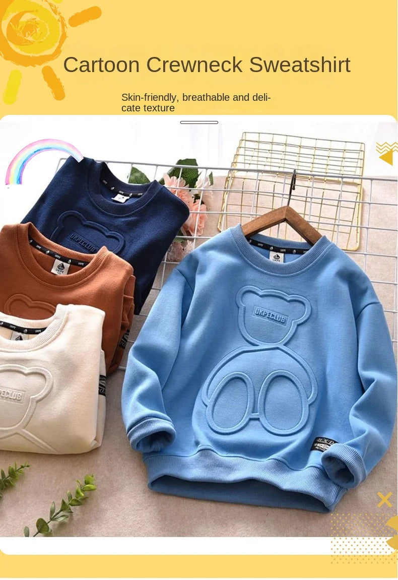 A light blue cartoon bear pullover sweatshirt displayed on a wooden hanger with other colored sweatshirts in the background.