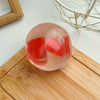 A clear pink squishy stress ball filled with red fruit shapes resting on a wooden cutting board.