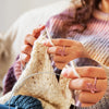Hands knitting a light beige yarn using an adjustable cat-ear yarn guide ring.