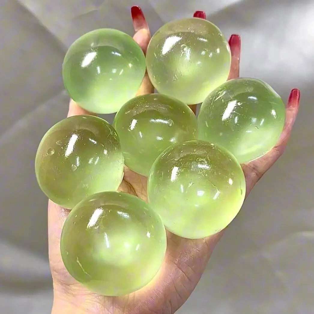 A hand holds six translucent light green slow rebound squeeze balls for stress relief.