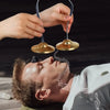 Hands are holding brass tingsha cymbals above a man's face, illustrating auspicious symbols.
