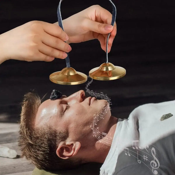 Hands are holding brass tingsha cymbals above a man's face, illustrating auspicious symbols.