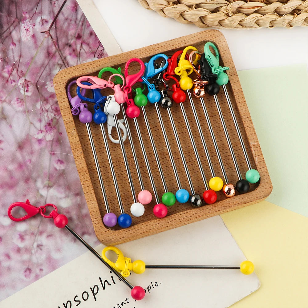A wooden tray holds various metal keychain bars with lobster clasps in colorful and silver tones for DIY jewelry making.