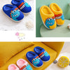 A collection of pink, blue, and yellow cartoon dinosaur plush slippers displayed on a yellow fabric.