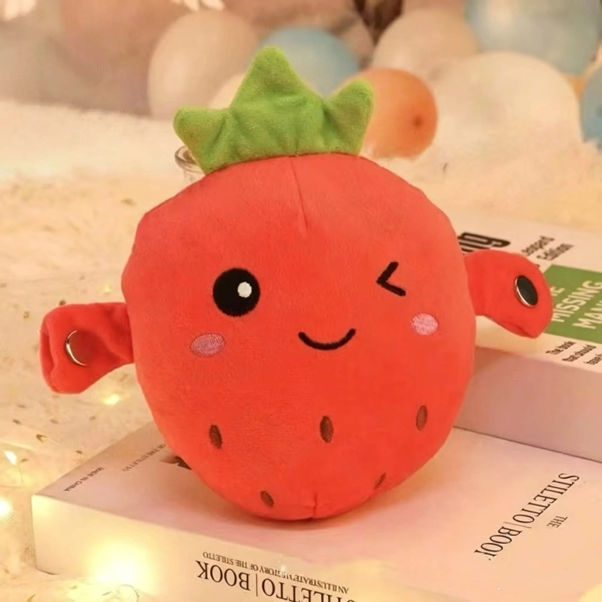 An orange strawberry plush toy with green leaves resting on a book.