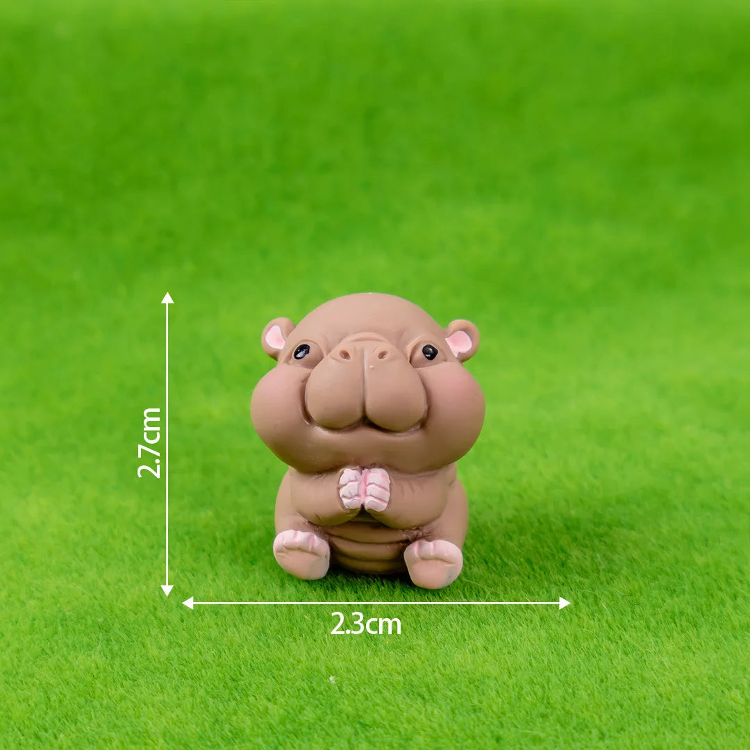 A small, light brown resin figurine of a hippo with pink accents, sitting on green grass.