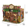A detailed miniature dollhouse kit featuring a wooden facade, greenery, and decorative elements.