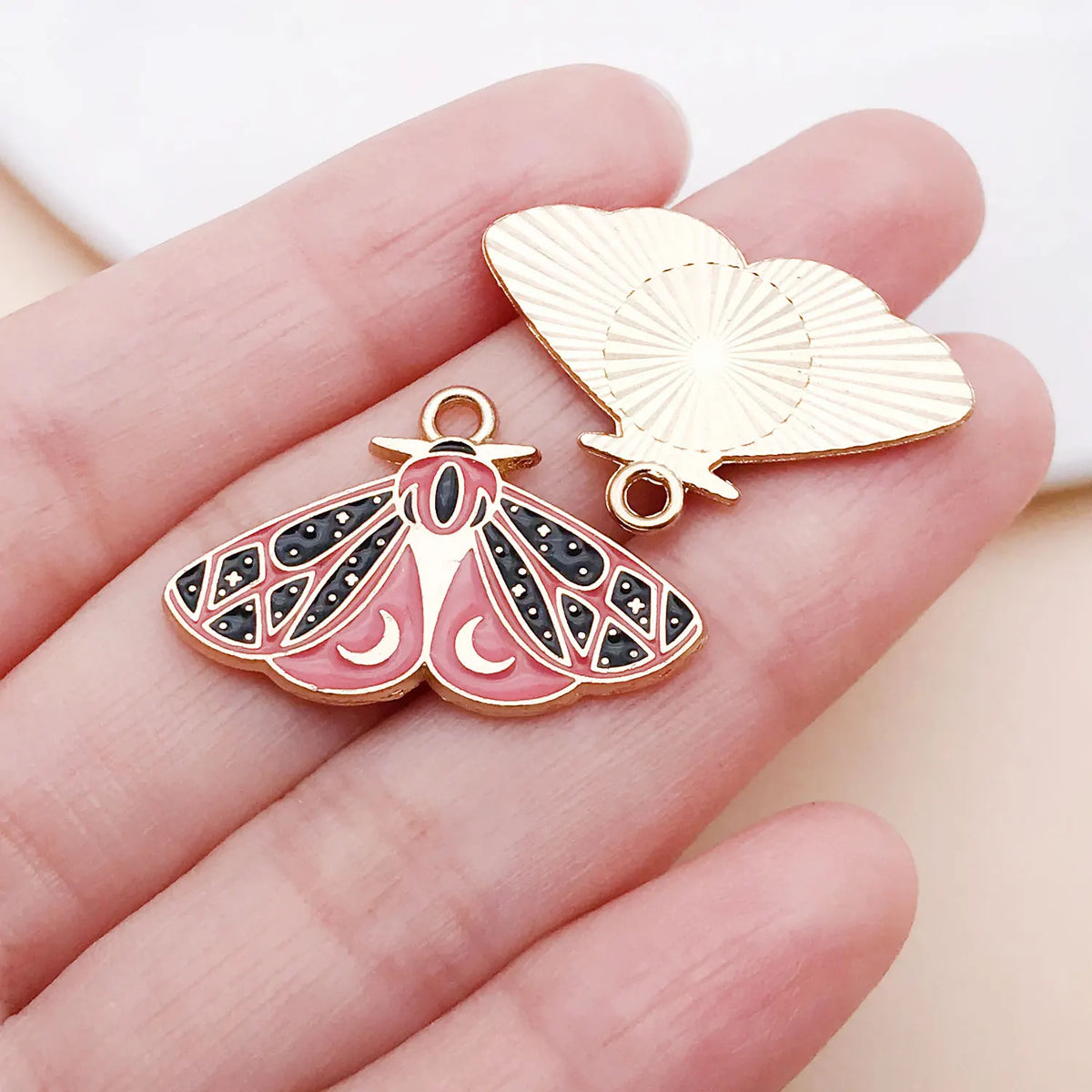Gold-toned butterfly drop charm with intricate patterns resting on a hand.