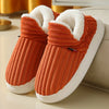 A pair of orange knitted slippers with white soles and faux fur lining resting on a light surface.
