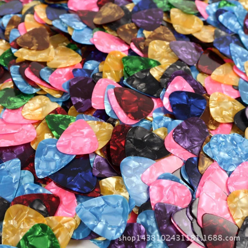 A close-up view of a 10-pack of assorted colored celluloid guitar picks scattered on a white surface.
