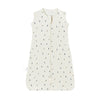 A cream colored sleeveless baby sleeping bag with a vertical zipper decorated with small evergreen trees.