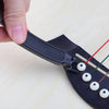 A hand is using a black tool to wind, cut, or pull guitar strings from a fretboard.