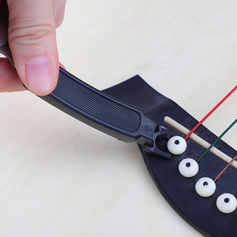 A hand is using a black tool to wind, cut, or pull guitar strings from a fretboard.