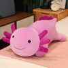 A soft pink axolotl plush pillow with purple fins resting on a light pink surface.