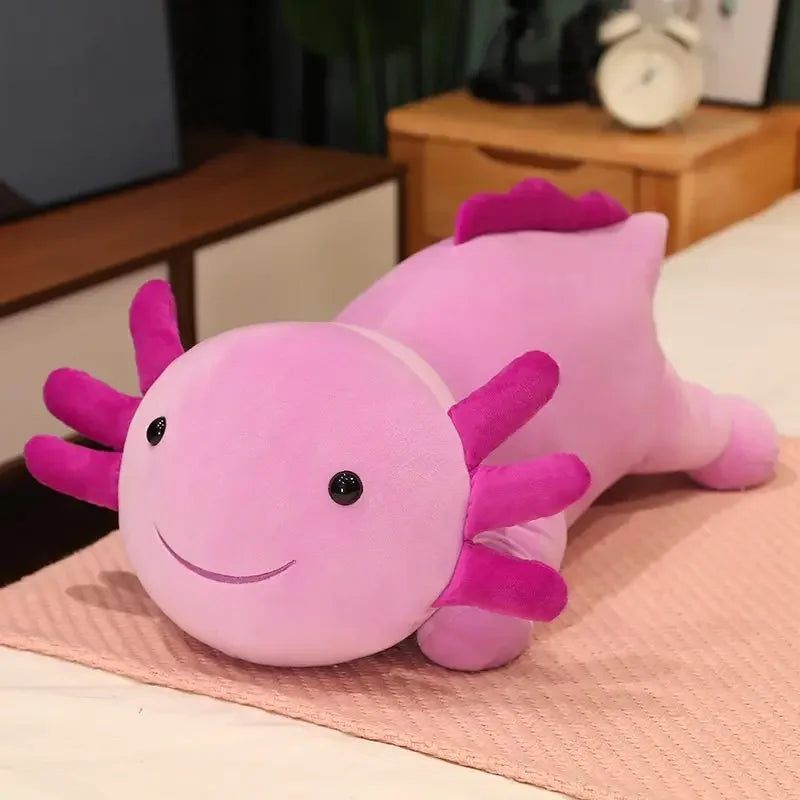 A soft pink axolotl plush pillow with purple fins resting on a light pink surface.