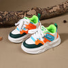 A pair of boys' breathable casual sneakers featuring white, orange, and teal accents with hook-and-loop straps resting on a b