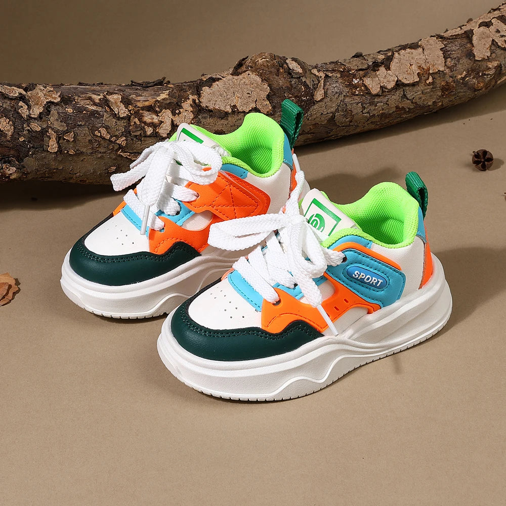 A pair of boys' breathable casual sneakers featuring white, orange, and teal accents with hook-and-loop straps resting on a b