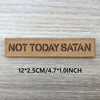 Un patch tissé beige rectangulaire avec le texte NOT TODAY SATAN sur une surface en bois gris.