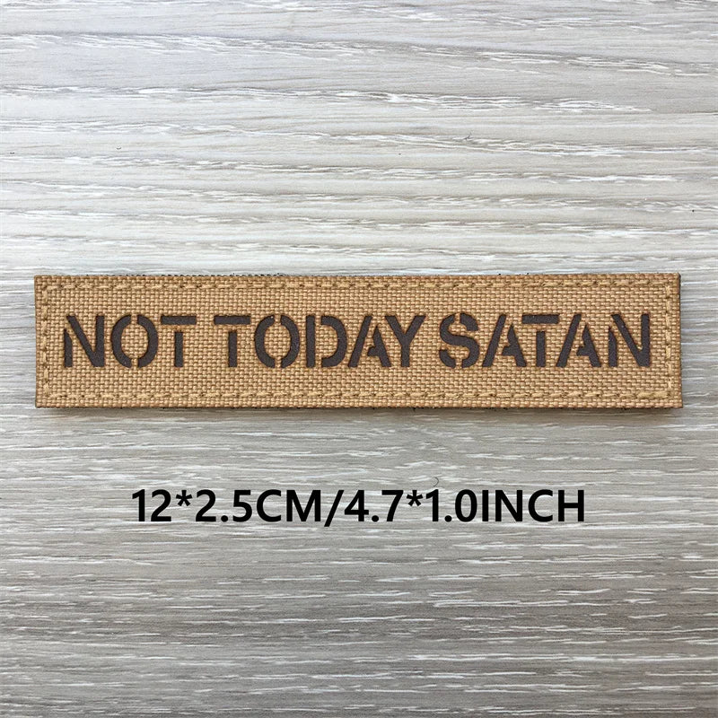 Un patch tissé beige rectangulaire avec le texte NOT TODAY SATAN sur une surface en bois gris.