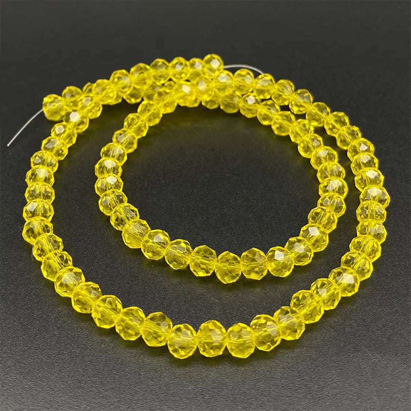 A strand of yellow Austrian faceted crystal beads for jewelry making laid out on a dark surface.