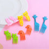 A set of colorful kawaii mini fruit forks in yellow, pink, orange, and blue against a pink background.