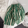 Green and beige striped cotton harem pants for kids laid out on a white surface.