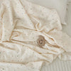 A cream colored muslin swaddle blanket with a subtle floral print is draped on a light surface.
