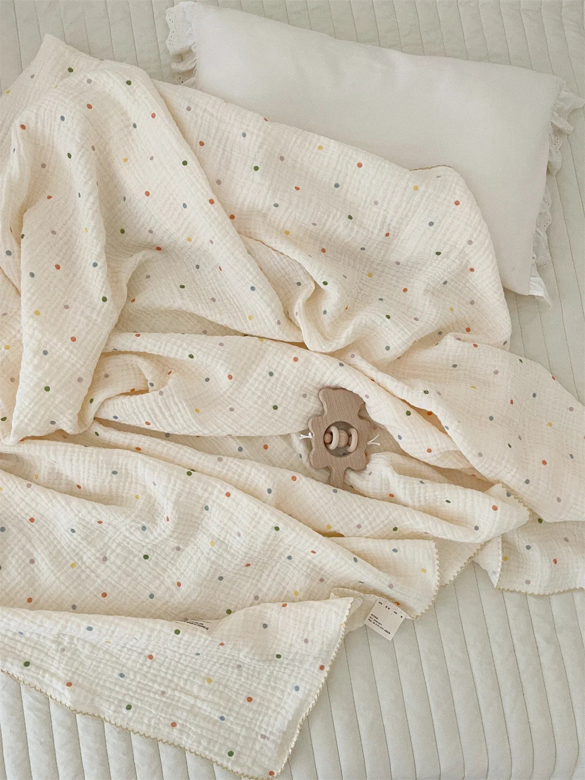 A cream colored muslin swaddle blanket with a subtle floral print is draped on a light surface.