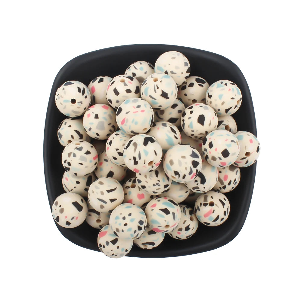 A black bowl filled with small, round silicone beads printed with leopard and daisy patterns.