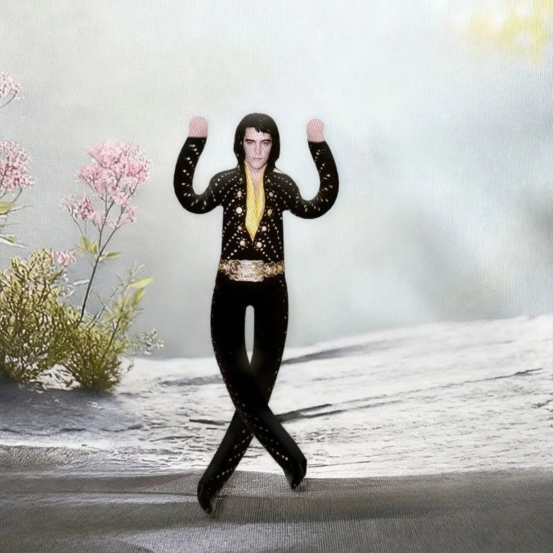 A plush doll resembling Elvis Presley with black attire and gold accents standing on a snowy surface.