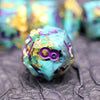 A teal resin polyhedral dice set with gold glitter accents resting on a dark surface.
