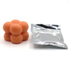A pile of orange candle dye chips for soy wax, beeswax, and paraffin, next to a small plastic bag.