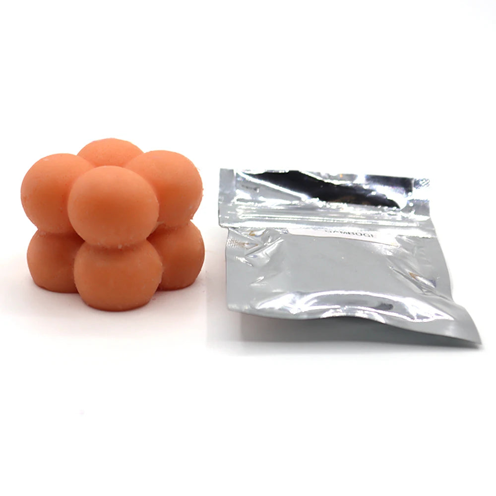 A pile of orange candle dye chips for soy wax, beeswax, and paraffin, next to a small plastic bag.