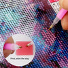 A close-up of a hand applying pink clay to a diamond painting surface with a pink applicator tool.