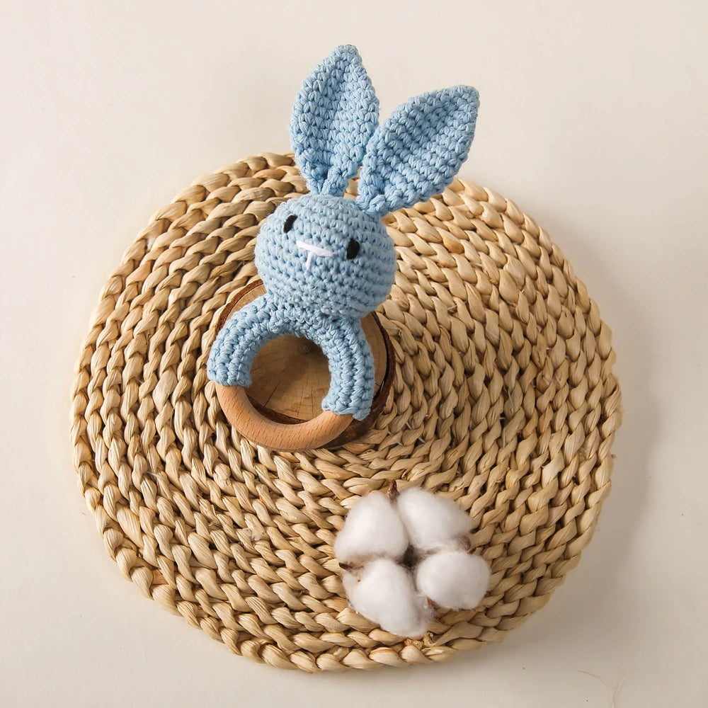 A light blue handmade crochet bunny rattle resting on a woven natural fiber mat.