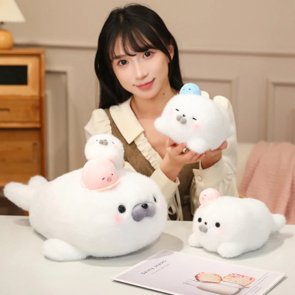 A white seal plush toy with a pink octopus hat is held by a woman on a table.