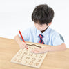A young boy is tracing letters on a wooden Montessori letter tracing board with a red pencil.