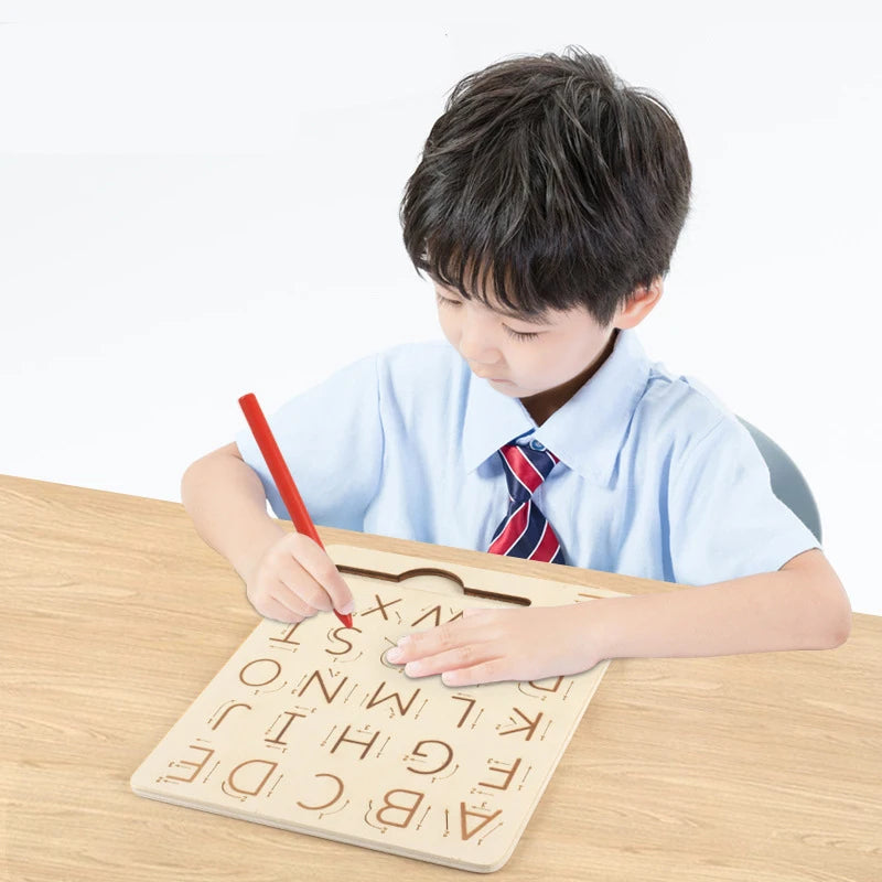 A young boy is tracing letters on a wooden Montessori letter tracing board with a red pencil.