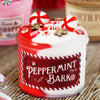 A red jar of peppermint bark candy with white frosting and red striped decorations sits on a burlap surface.
