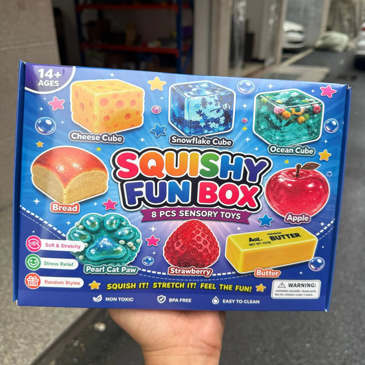Eine Box mit Squishy Fun Box sensorischen Spielzeugen, darunter Käse-, Schneeflocken-, Ozean-Cube, Brot, Apfel und Erdbeere.