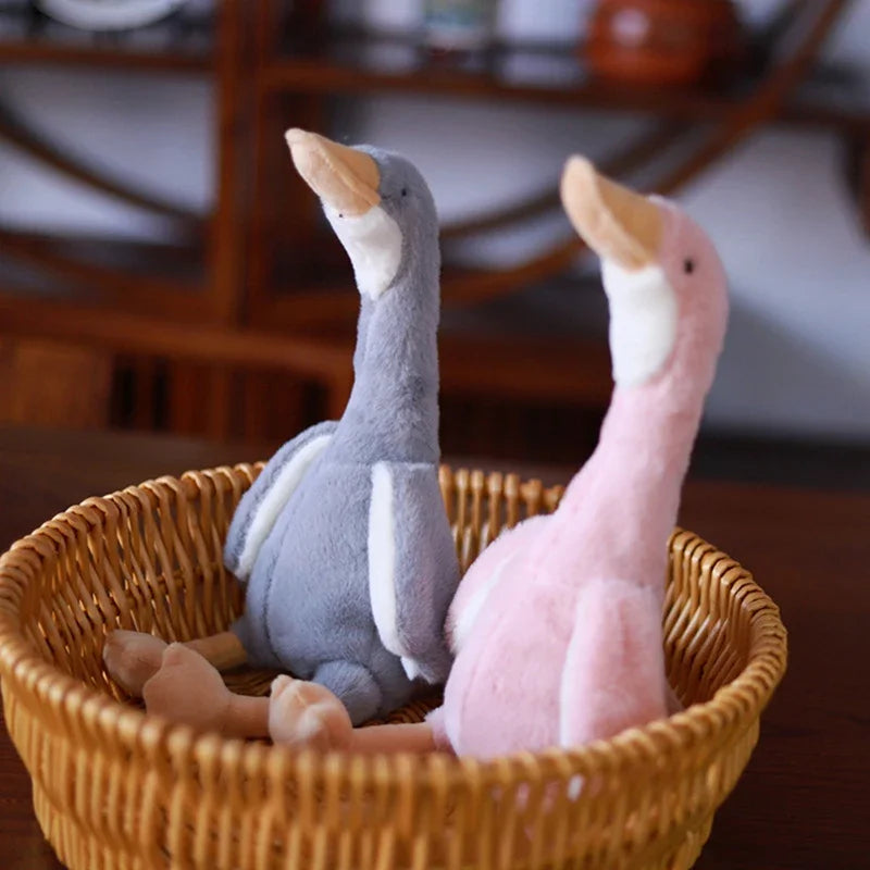 A pair of soft plush toys resembling long-necked geese in gray and pink colors are displayed in a woven basket.