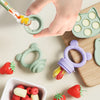 A hand is using a silicone baby fruit feeder set with freezer molds to feed a strawberry and other fruits.