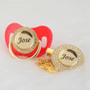 A red pacifier and clip gift set featuring a gold-toned ring with a crystal disc engraved with the name Jose