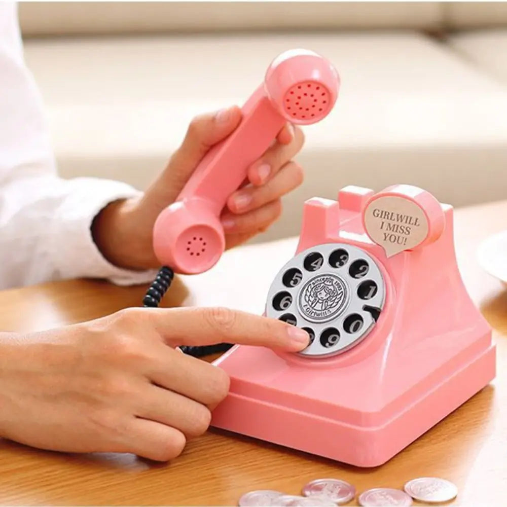 A hand is placing a coin into a pink vintage rotary telephone piggy bank for savings.