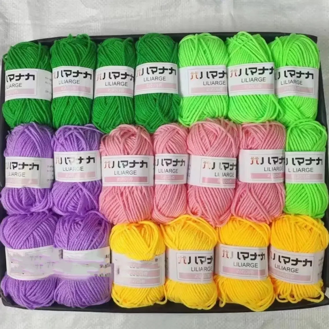 A variety pack of bright colored acrylic yarn skeins in shades of green, pink, yellow, and purple for knitting and crochet pr