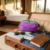 A brown leather suitcase opens to reveal a purple alpaca themed travel storage bag, sunglasses, and a passport.