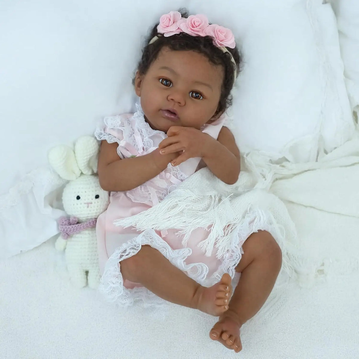 A baby with a floral headband and a white bunny toy is lying on a white surface.