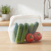 Clear silicone storage bag filled with fresh green cucumbers and red tomatoes on a wooden surface